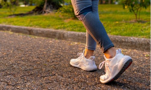 Immagine delle gambe di una donna che cammina sull'asfalto per capire quanti passi fare al giorno per stare in salute