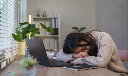 Ragazza sdraiata con il viso sul tavolo e il pc davanti a sé per la stanchezza da smarworking
