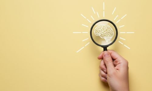 Lente di ingrandimento su sfondo giallo che inquadra il disegno di un cervello stilizzato