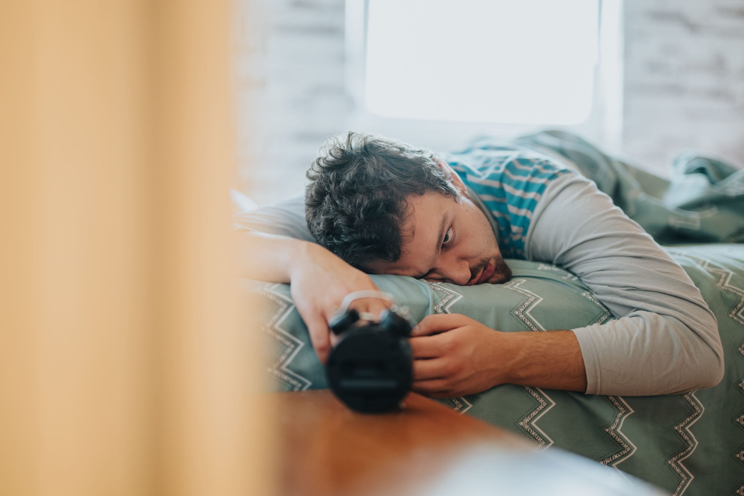 Uomo sdraiato sul letto che guarda la sveglia con espressione turbata a causa di cpk alto e stanchezza